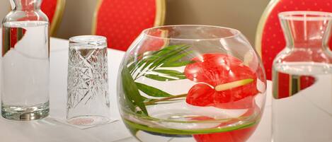 Una mesa con tres jarrones de vidrio transparente, uno con una flor roja y hojas verdes, y dos jarrones vacíos.