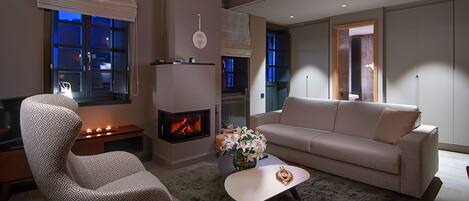 Una sala de estar moderna con chimenea, un sofá, un sillón estampado y una mesa de centro con un jarrón de flores.