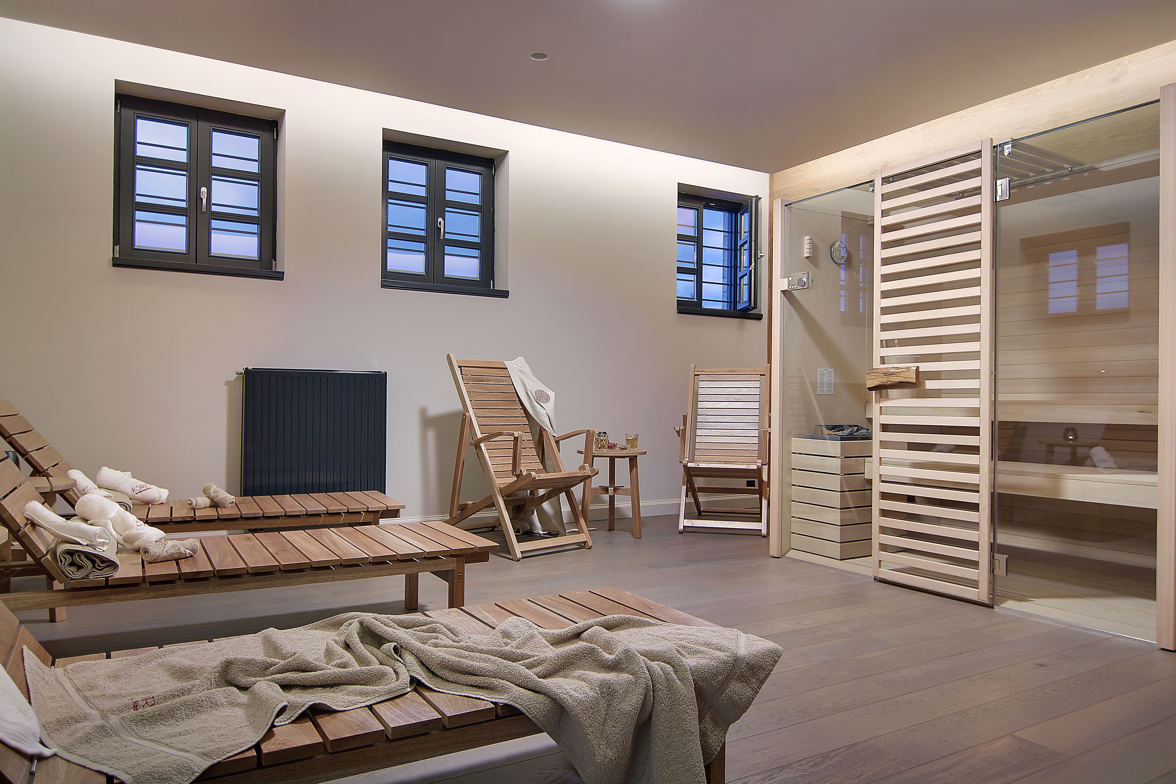 Una habitación con sillones de madera, un radiador y un ventanal corredero que da a un baño.
