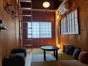 Una habitación tradicional japonesa con suelo de tatami, una mesita baja, cojines, una escalera y puertas correderas.