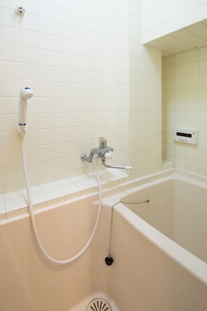 Una bañera blanca con un cabezal de ducha manual y un panel de control en la pared.
