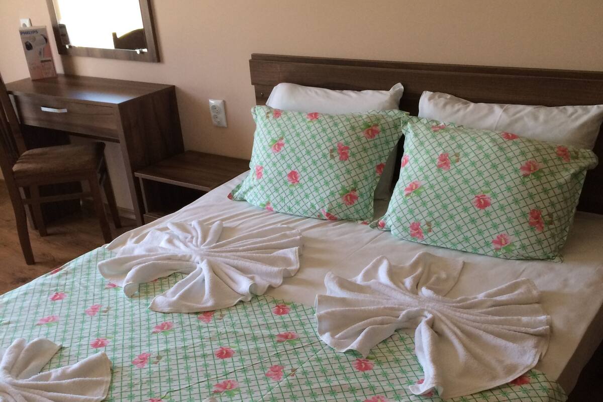 Un lit bien fait, avec une literie et des serviettes à motifs floraux disposées de manière décorative.