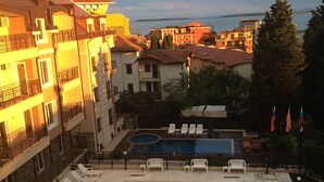 Une piscine entourée de chaises longues, elle-même bordée d’immeubles dotés de balcons et offrant une vue sur la mer.