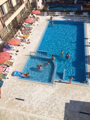 A swimming pool with multiple people, sun loungers, and umbrellas. - Horizont Apartments (Sunny Beach)