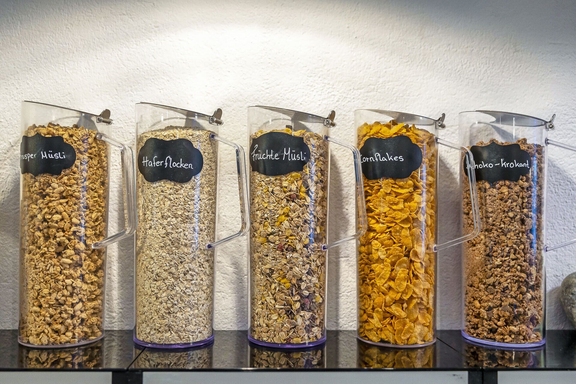 Five labeled containers of different cereal flakes.