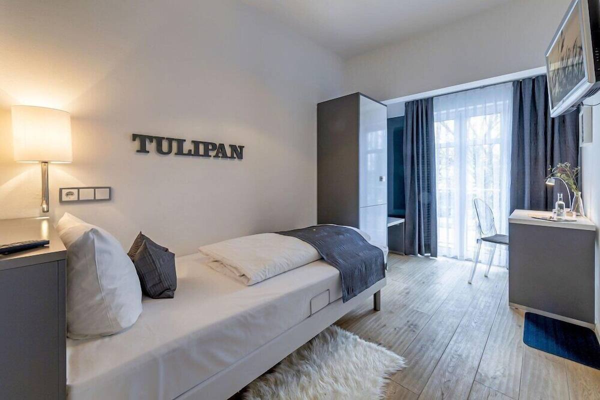 A modern bedroom with a bed, a nightstand, a lamp, a desk, and a chair.