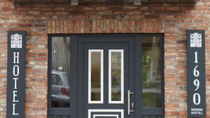 A modern hotel entrance with a black door, two potted plants, and signage indicating the hotel's name and address.