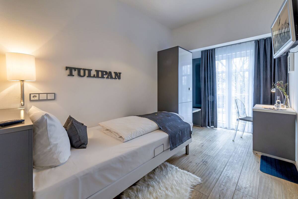 A modern bedroom with a bed, a nightstand, a lamp, and a wall-mounted TV.