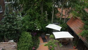 An outdoor patio area with a wooden deck, a seating area with a table and chairs, and a large white umbrella providing shade.