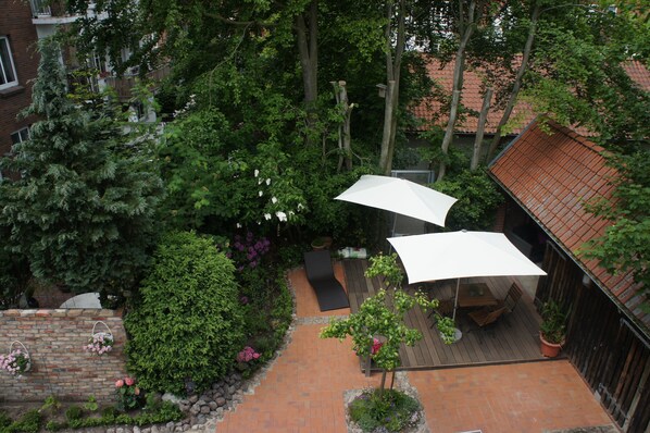 Un área de patio al aire libre con cubierta de madera, un espacio de descanso con mesa y sillas, y un amplio paraguas blanco que da sombra.