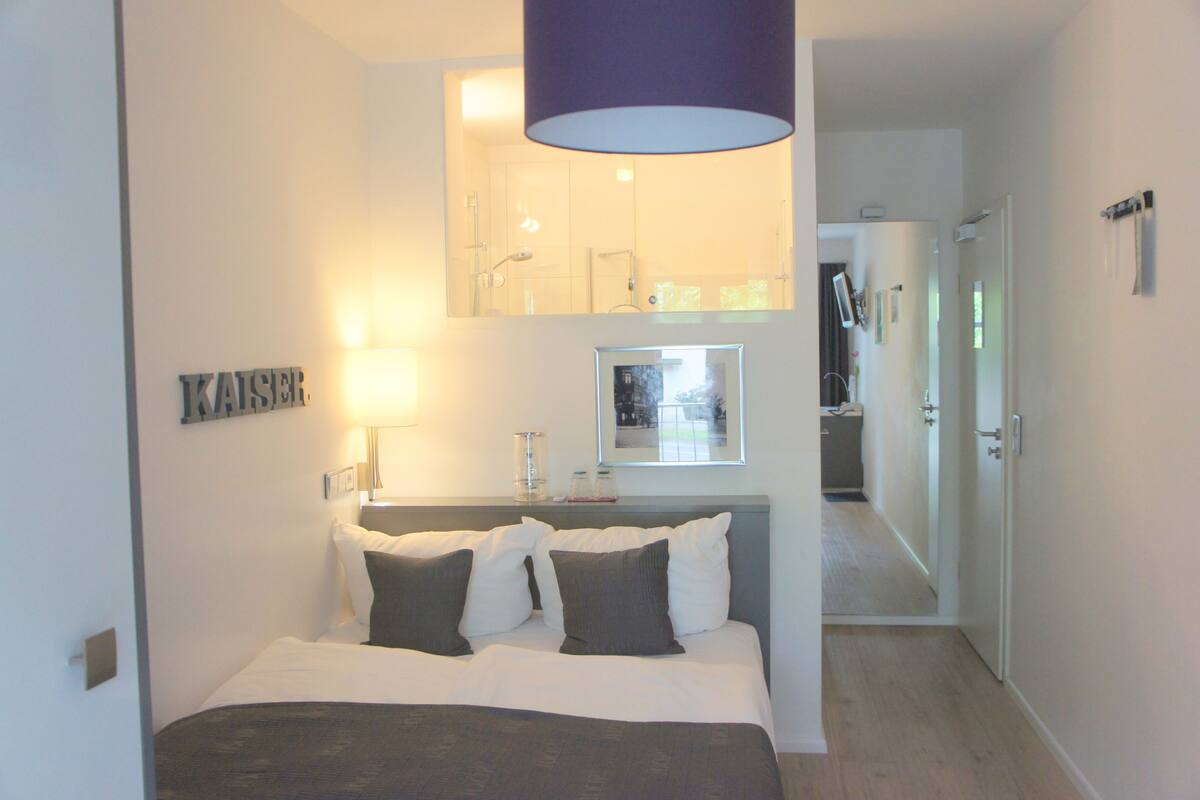 A hotel room with a bed, a mirror, a window, and a door.