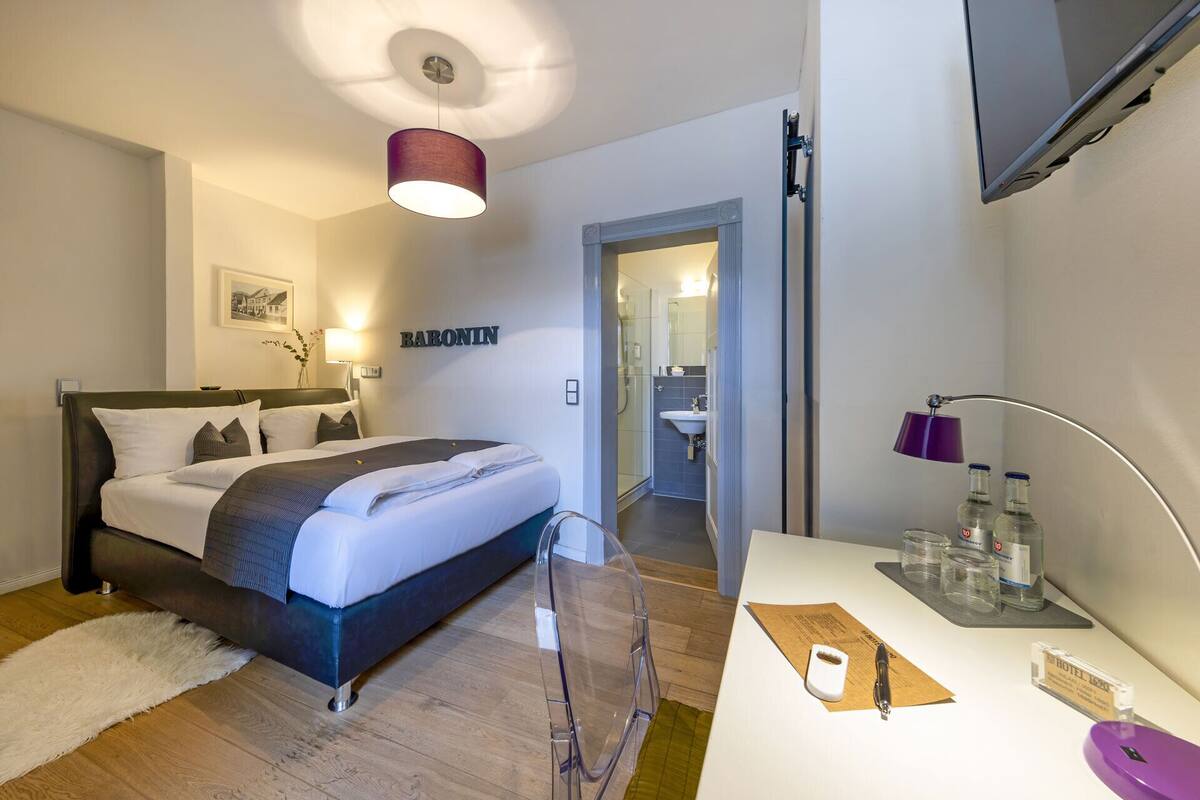 A hotel room with a bed, bedside table, lamp, and a mirror.