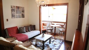 Un salon avec un canapé, une table basse et un lustre. Une fenêtre offre une vue sur l’extérieur.