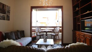 Un salon comprenant un canapé, deux fauteuils, une table basse, un lustre et un téléviseur.