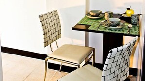 A small dining area with a table set for two, chairs with a checkered pattern, a mirror above the table, and a kitchen visible in the background. - 2F6 Wharton Bldg North Cambridge Condo (Baguio)