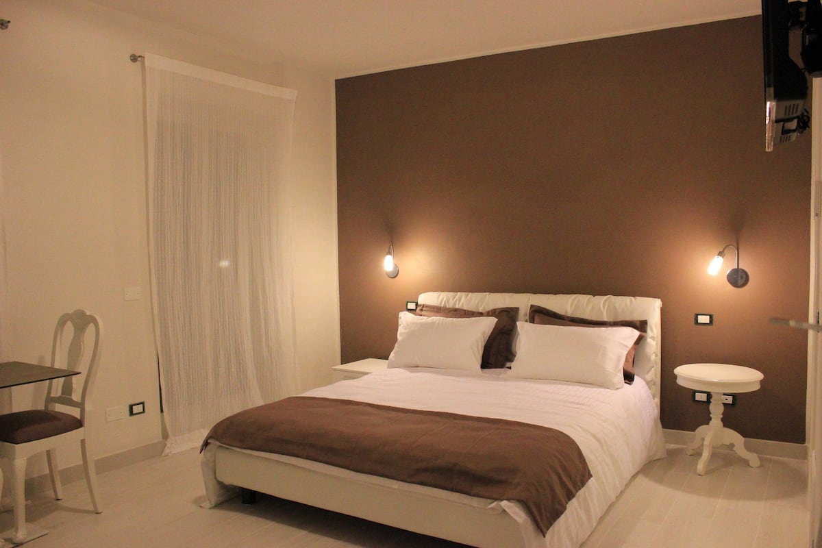 Une chambre à coucher avec un lit, des tables de chevet, une chaise et un rideau.