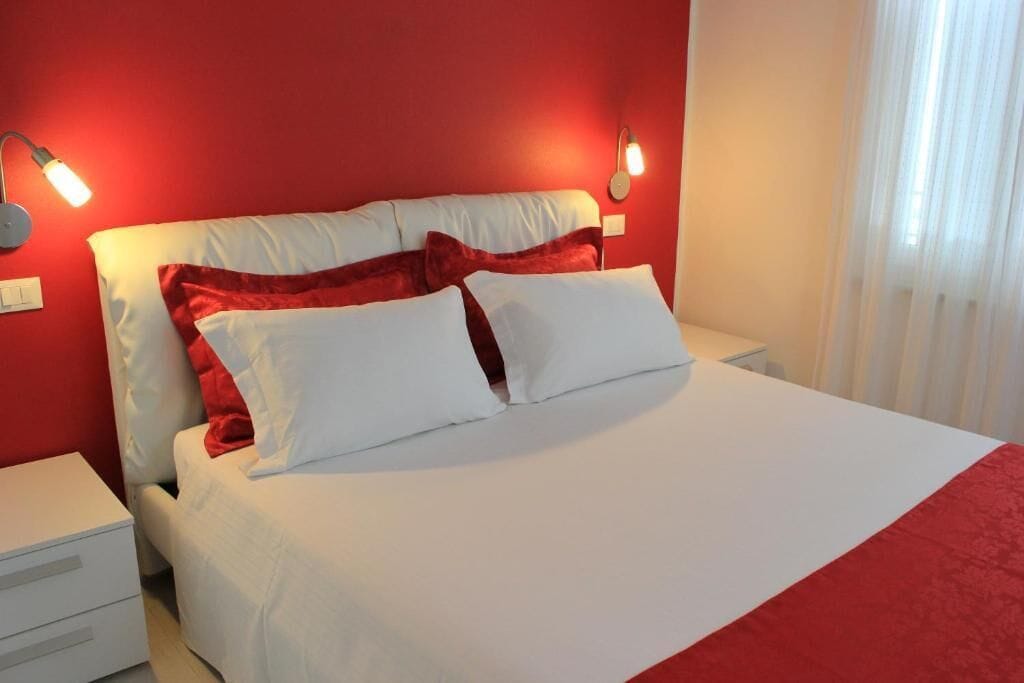 A bed with white and red bedding, two bedside tables, and red walls.