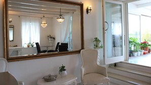 Une pièce avec un grand miroir, une chaise, une petite table avec une plante, et une vue sur un balcon orné de plantes en pot.