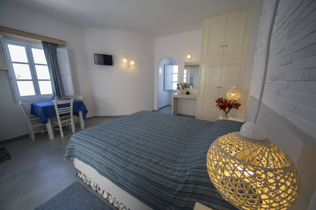 Un dormitorio con cama, escritorio y silla, cómoda, espejo y lámpara colgante.