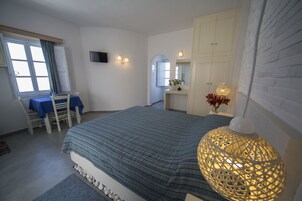 Un dormitorio con cama, escritorio y silla, cómoda, espejo y lámpara colgante.