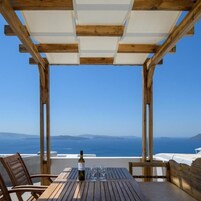 Una pérgola de madera con una mesa y sillas que dan a una vista panorámica del mar y la costa lejana.