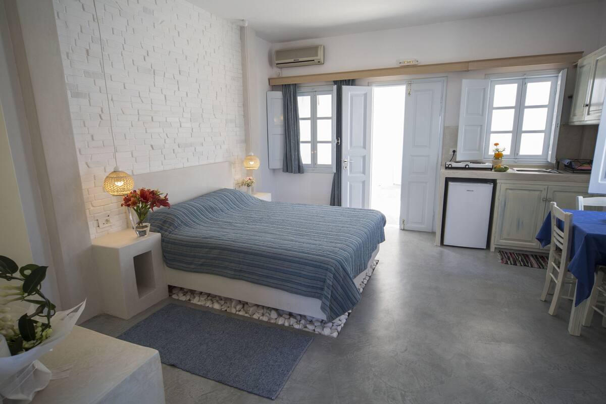 Un dormitorio con cama, mesita de noche, lámpara y una pequeña mesa con un florero.