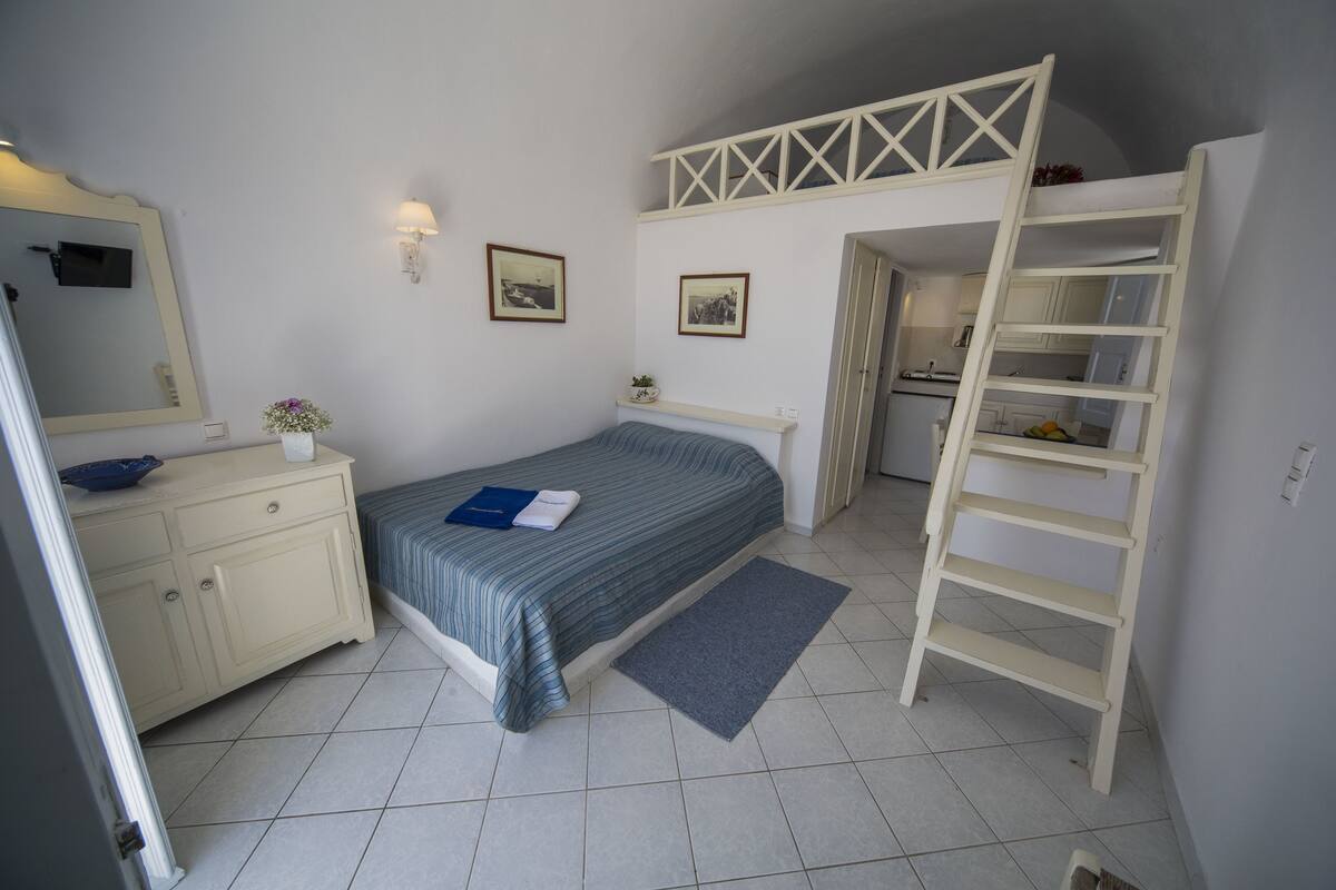 Un dormitorio con cama, cómoda, espejo y escalera que lleva a una zona elevada.