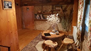 Una habitació de fusta acollidora amb una taula rodona, dos tamborets, una biblioteca i un vas amb flors seques.