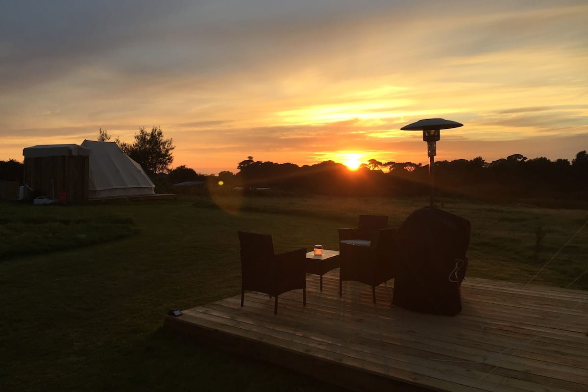 A wooden deck with a table and chairs, a grill, and a tent in the background.