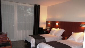 Een hotelkamer met twee bedden, een bureau met stoel en een groot raam met gordijnen.