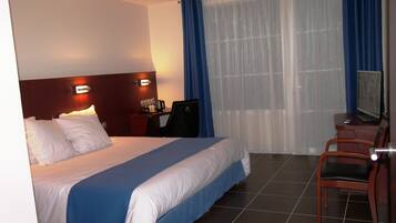 Una habitación de hotel con cama, escritorio, silla, televisor y ventana con cortinas.