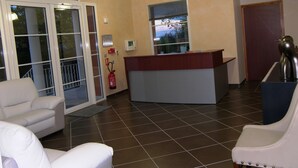 Een receptiegedeelte met een receptiebalie, twee witte lederen fauteuils, een brandblusser en uitzicht door het raam.