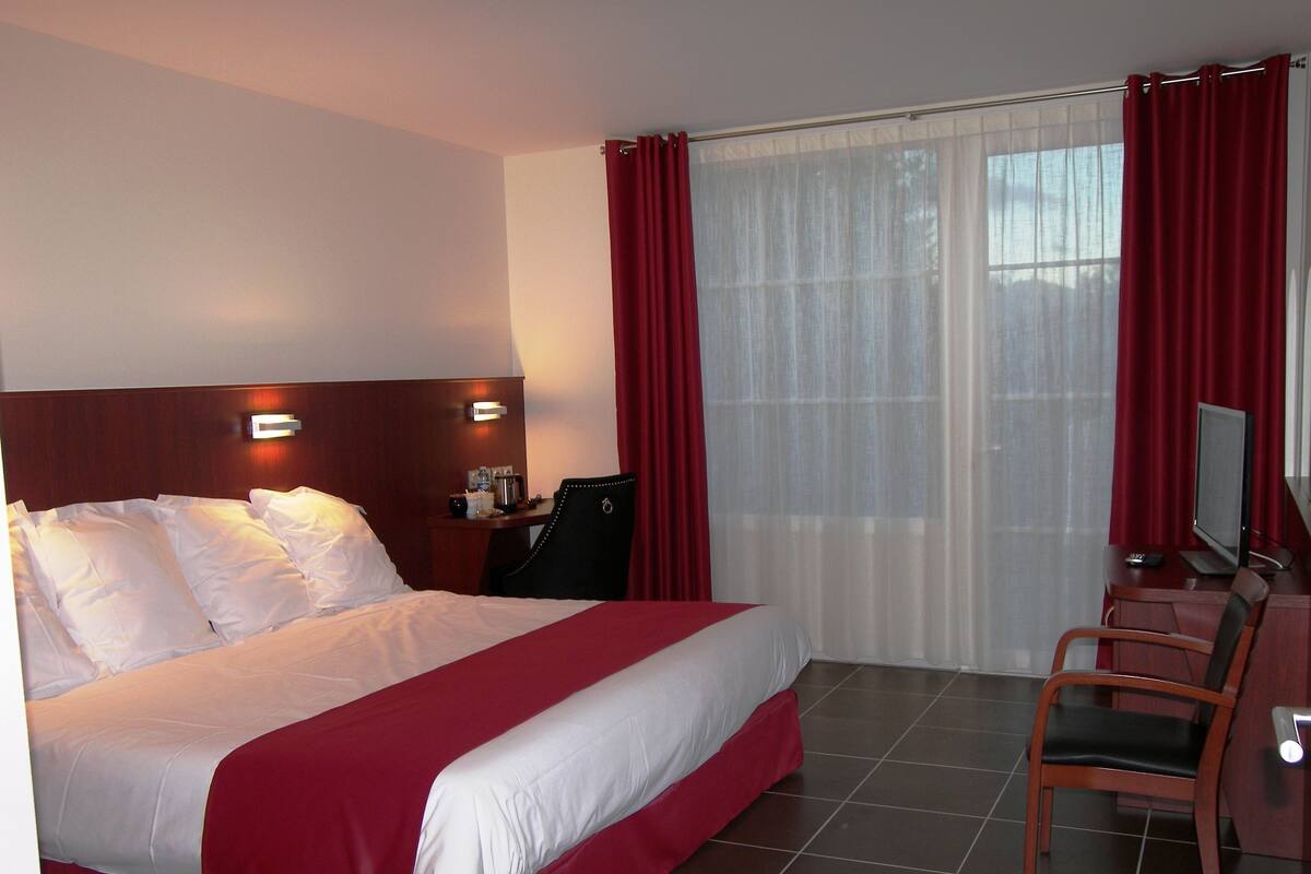 Quarto de hotel com uma cama grande, uma escrivaninha com computador e uma cadeira.