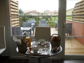 Uma bandeja de café da manhã com pão, suco e chá sobre uma mesa perto de uma janela com vista para móveis de jardim e vegetação.