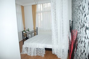Een slaapkamer met een bed, een radiator en een raam met dunne gordijnen.