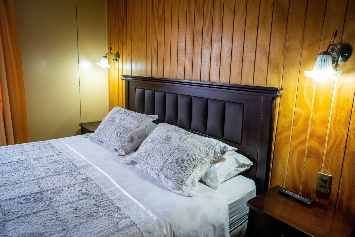 A neatly made bed with a dark headboard and two wall-mounted light fixtures.