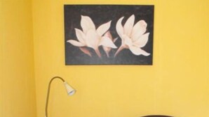 A room with a yellow wall, a painting of flowers, a desk with a lamp, and two dark armchairs. - Marco's Heuboden (Oberzissen)