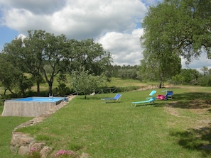A pool area with blue lounge chairs, a stone wall, and a grassy field with trees.