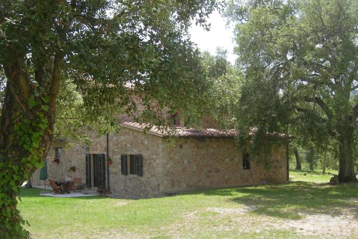 Un bâtiment en pierre, doté d’un toit en tuiles, entouré d’arbres et d’herbe.