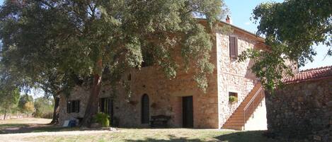 A stone building with a staircase leading to a second floor, surrounded by trees.