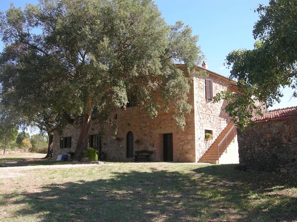 A stone building with a staircase leading to a second floor, surrounded by trees.