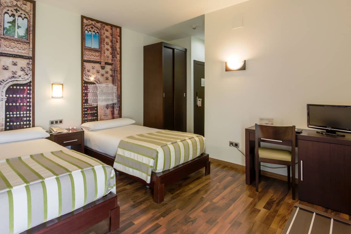 Habitación de hotel con dos camas, un escritorio con silla, televisor y armario.