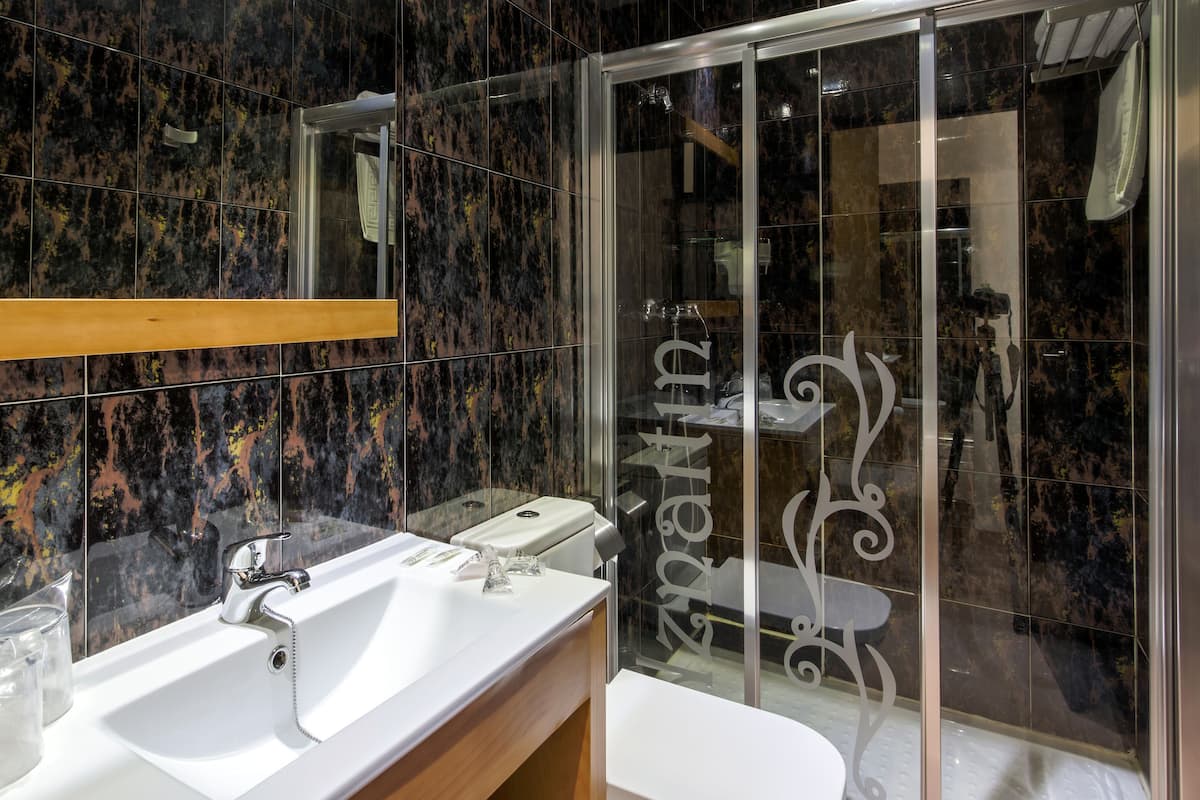 Un baño moderno con lavamanos blanco, cabina de ducha con mampara de cristal y pared revestida de mármol.