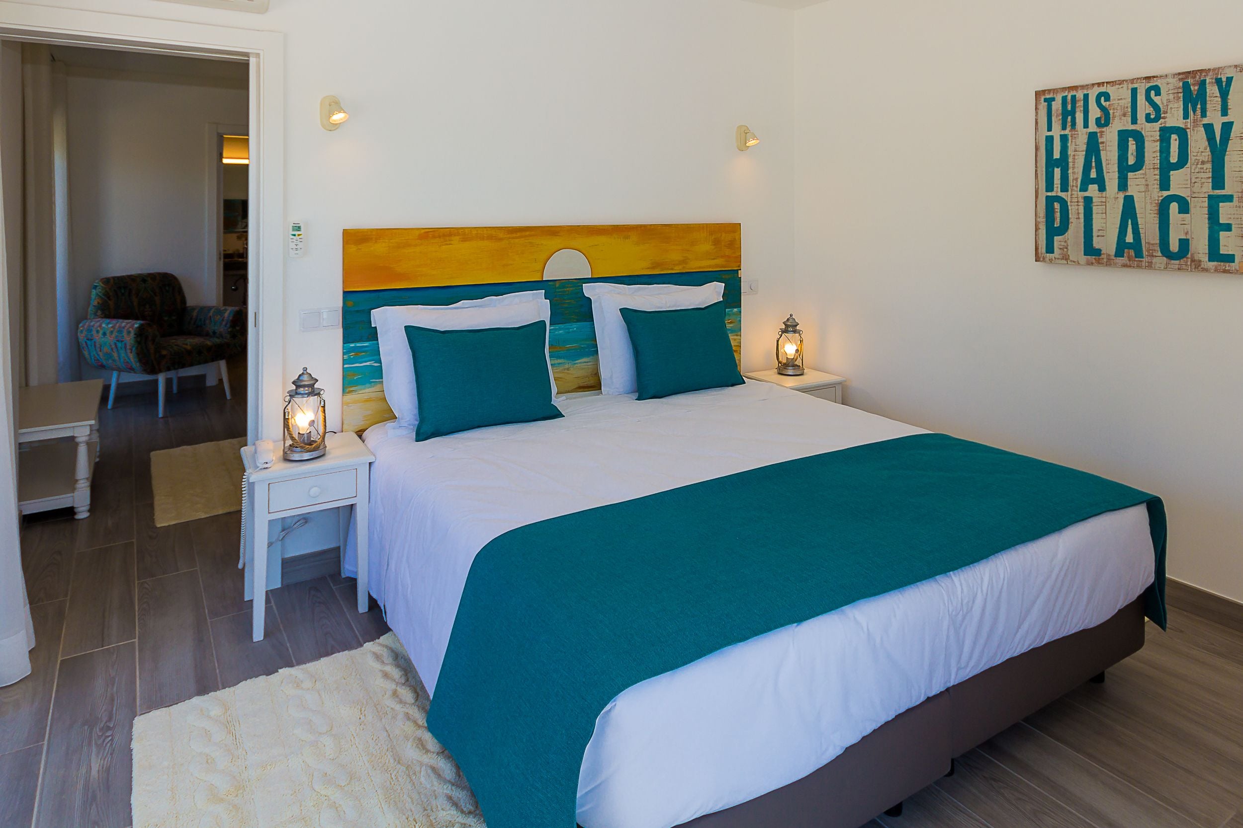 A bedroom with a large bed, two bedside tables with lamps, a chair, and a painting on the wall.
