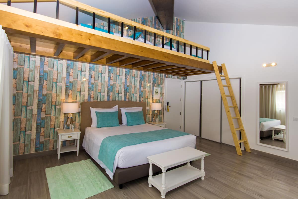 Ein Schlafzimmer mit Hochbett, Holzboden, grünem Teppich, Nachttisch und Spiegel.