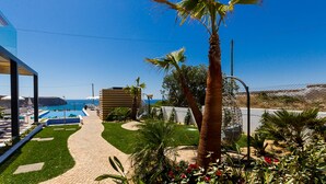 A pathway leading to a pool area with a view of the ocean, surrounded by palm trees and a fence.