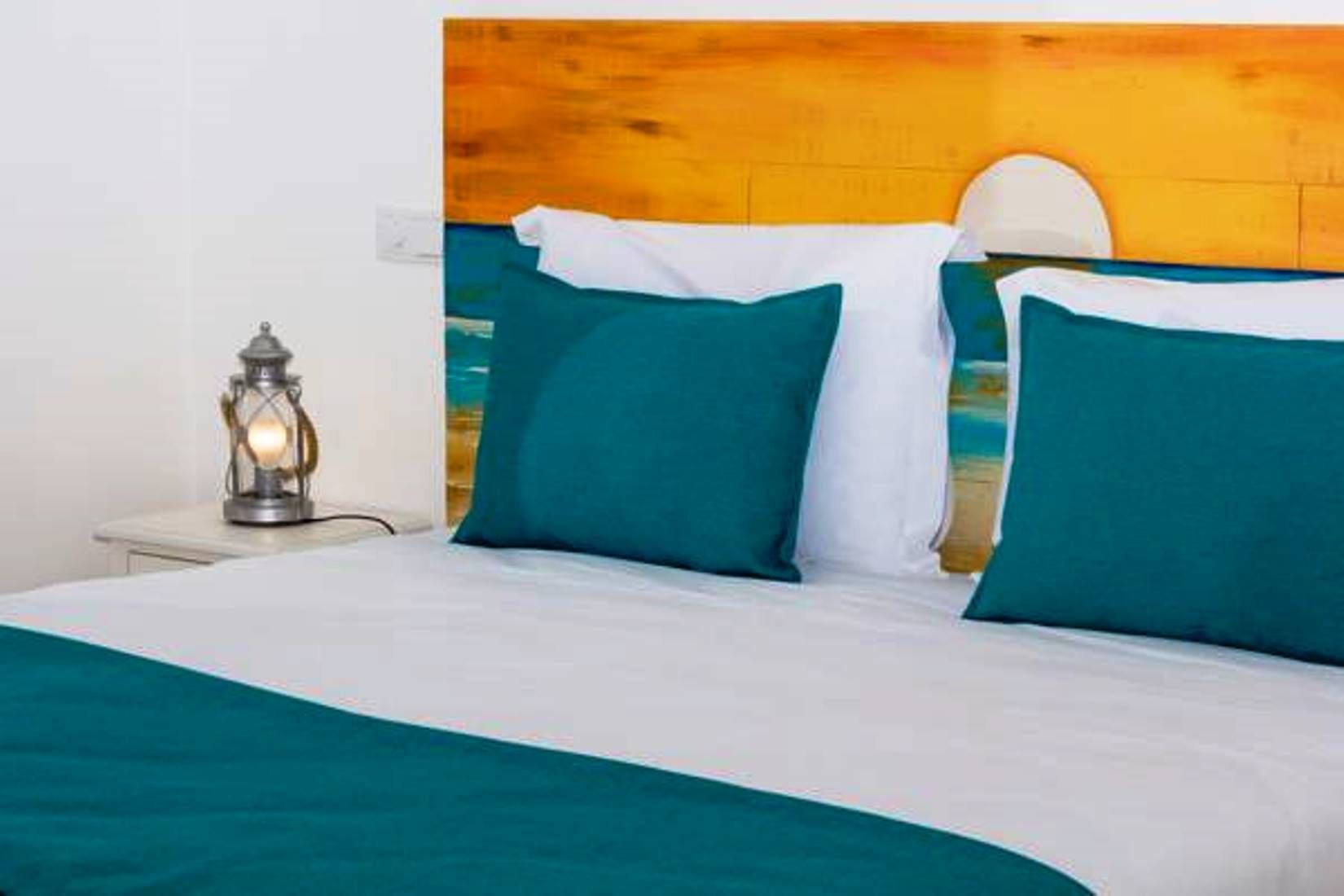 Een bed met smaragdgroene en witte beddengoed, een houten hoofdbord, en een wandlamp.