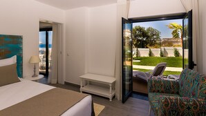 A hotel room with a bed, a chair, a small table, and a view of a garden through an open door.