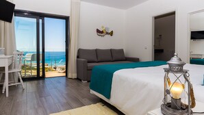 A bedroom with a bed, a nightstand, a lamp, a sofa, and a view of the ocean through a sliding glass door.