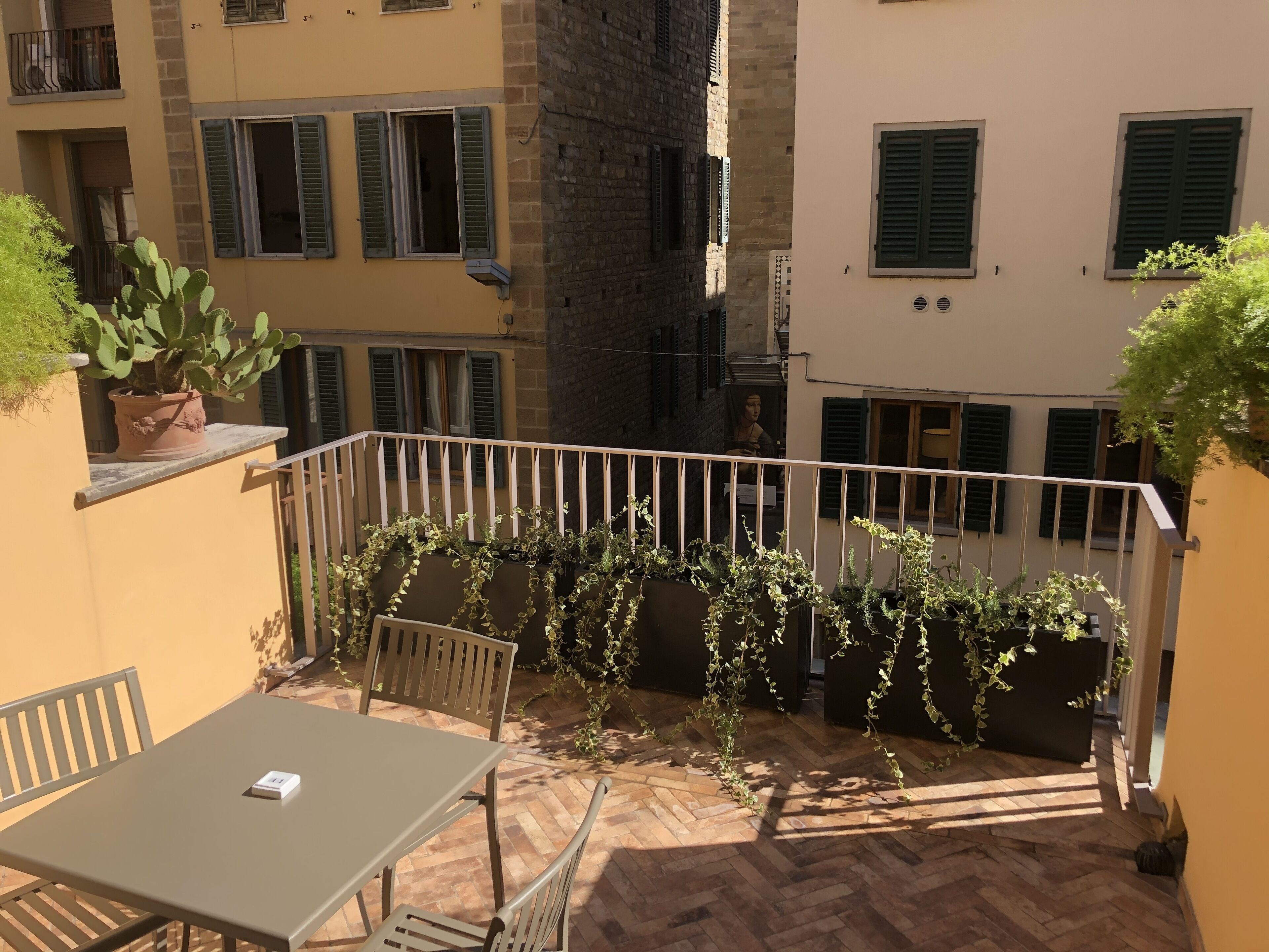 Un balcon avec une table et des chaises, entouré de plantes en pot et doté d’un sol au motif en chevrons.